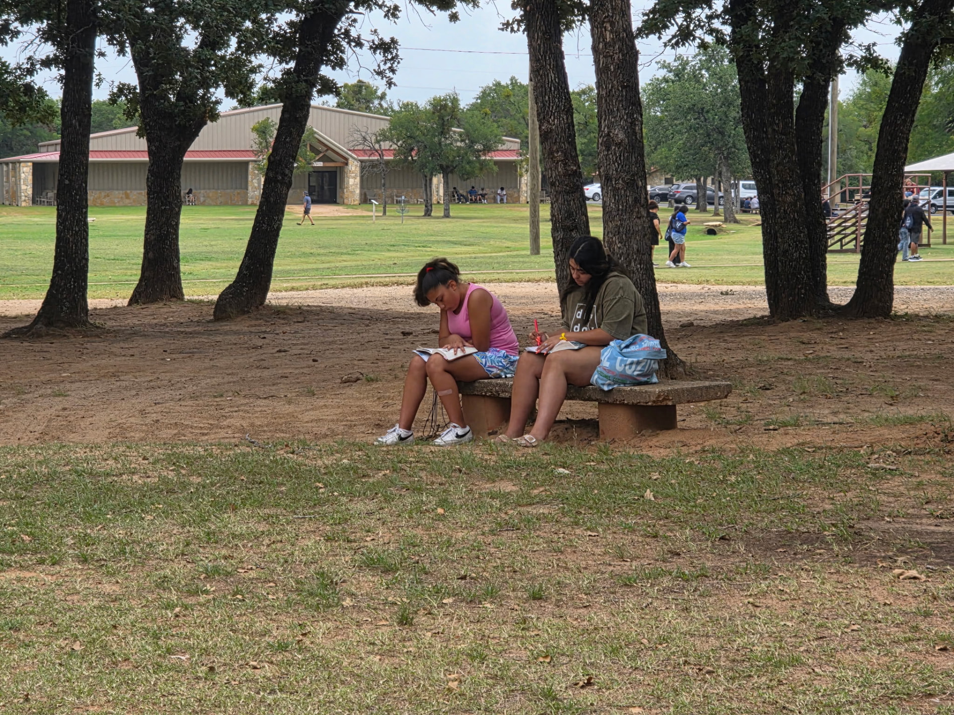 Two students doing their Bible study workbooks on a bench in the shade