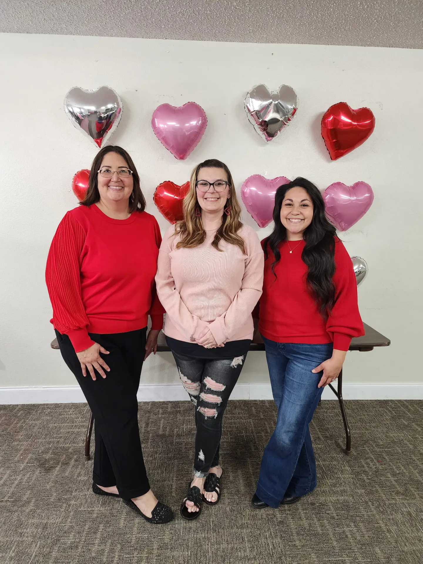 Three women from the church posing in front of heart balloons
