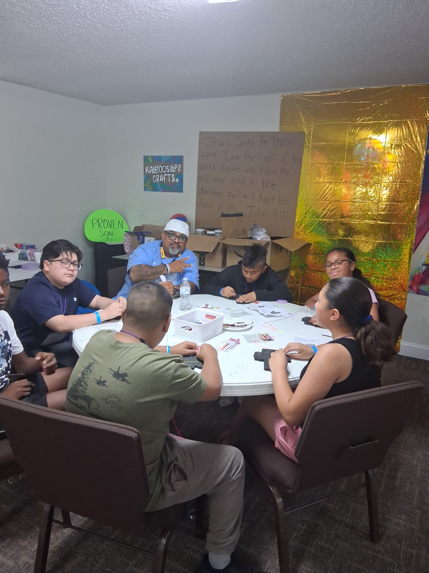 Kids making kaleidoscope crafts around a table with a volunteer
