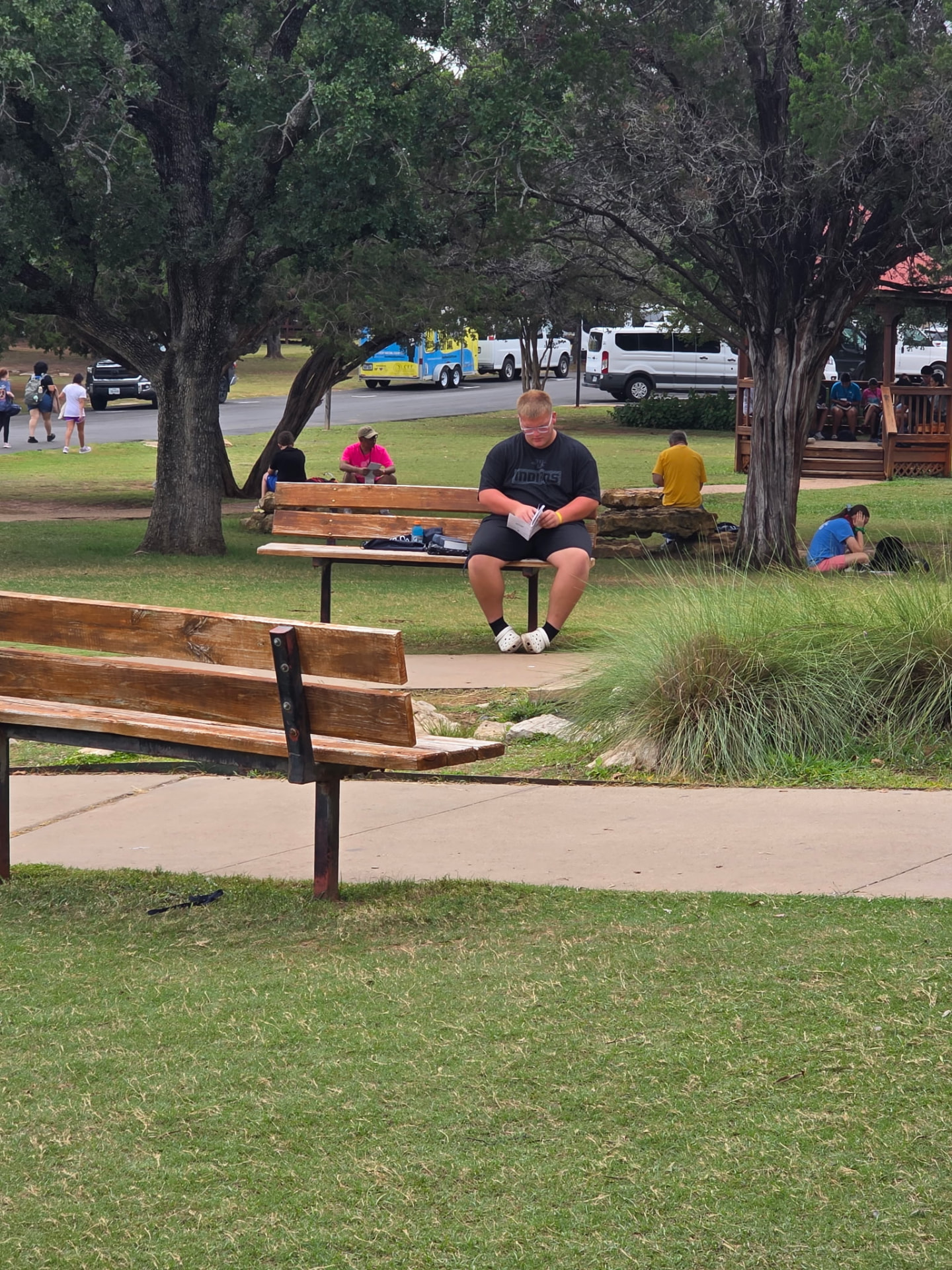 A student reading notes on a bench under the trees at camp